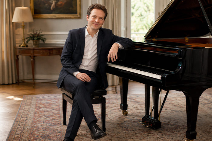 Professional pianist posing beside a grand piano in an elegant music room
